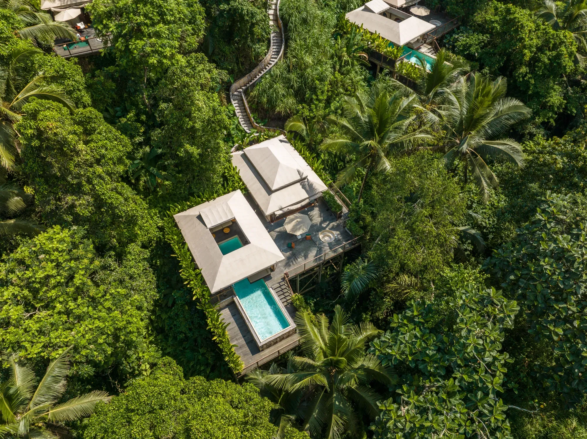 Aerial view of a luxury infinity pool lodge at Kanva Ubud, surrounded by lush tropical jungle and palm trees.